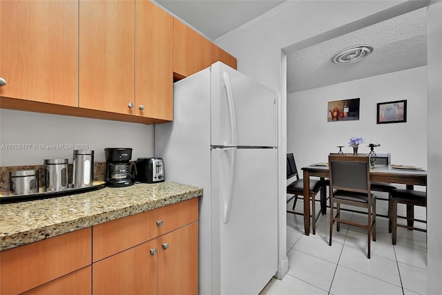 kitchen featuring white fridge, a textured ceiling, and light tile patterned floors