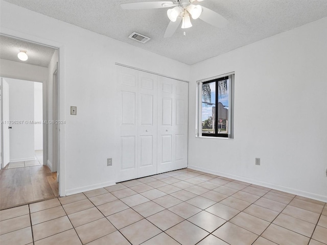 unfurnished bedroom featuring ceiling fan, light tile patterned floors, a textured ceiling, and a closet