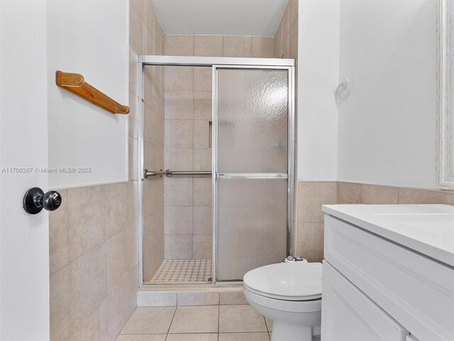 bathroom featuring tile patterned floors, toilet, a shower with door, vanity, and tile walls