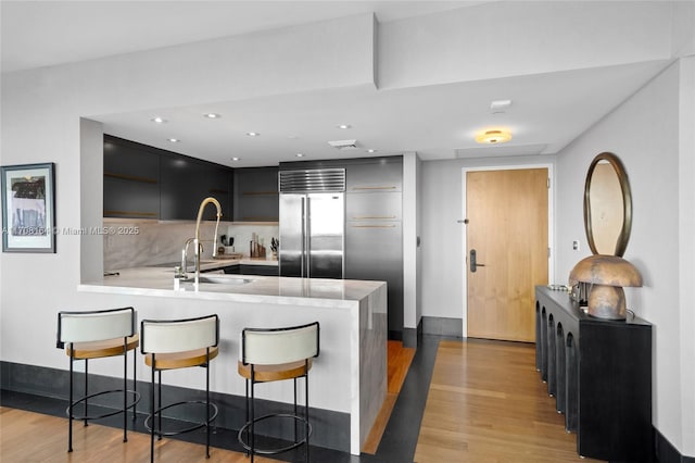 kitchen with light countertops, modern cabinets, light wood-type flooring, stainless steel built in refrigerator, and a peninsula