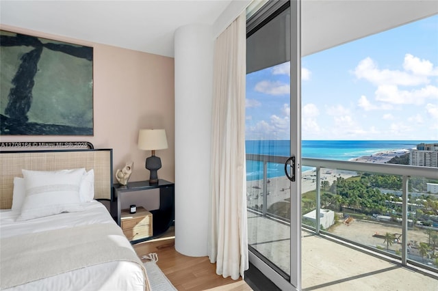 bedroom with a water view, access to exterior, a view of the beach, and wood finished floors