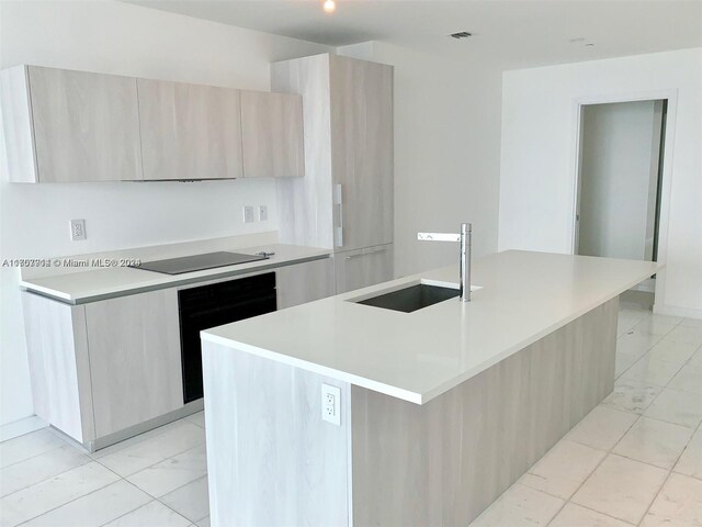 kitchen featuring black appliances, sink, a kitchen island with sink, and light brown cabinetry