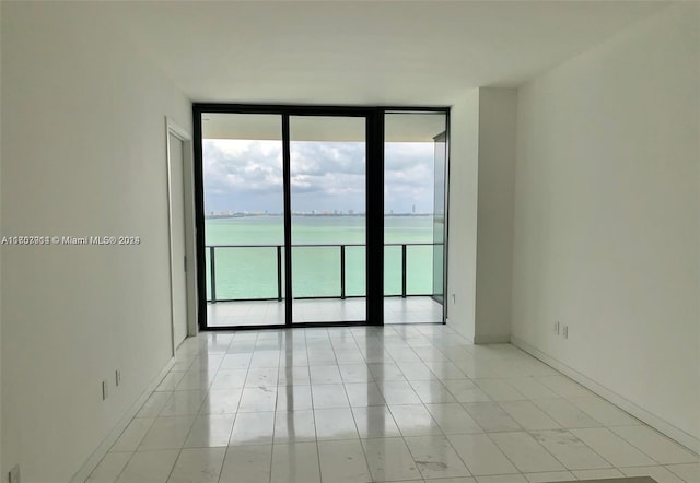 empty room with expansive windows, a water view, and light tile patterned floors