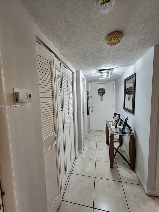 hall with a textured ceiling and light tile patterned flooring