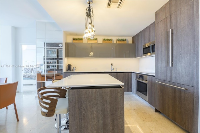 kitchen with appliances with stainless steel finishes, a kitchen breakfast bar, sink, a kitchen island, and hanging light fixtures