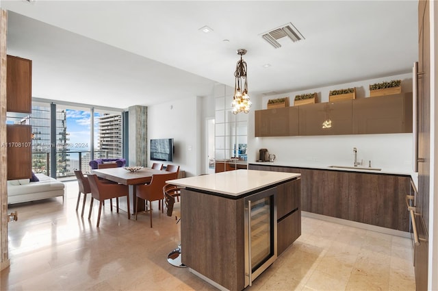 kitchen featuring expansive windows, a kitchen island, sink, wine cooler, and hanging light fixtures