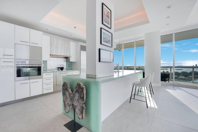 kitchen with sink, a kitchen island, a raised ceiling, oven, and white cabinets