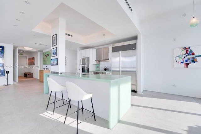 kitchen with a raised ceiling, kitchen peninsula, built in refrigerator, decorative light fixtures, and a breakfast bar area