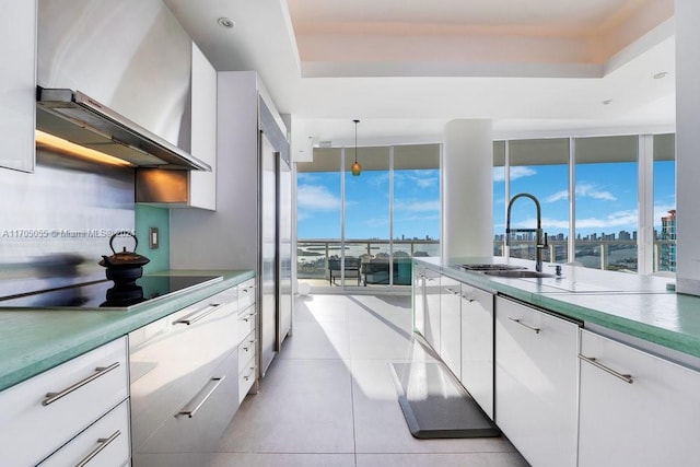 kitchen with wall chimney exhaust hood, black electric cooktop, sink, pendant lighting, and white cabinetry