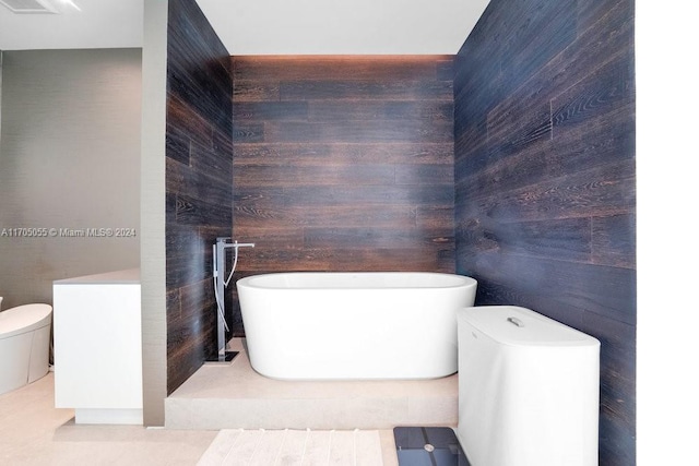 bathroom with a bathing tub, tile patterned flooring, toilet, and wooden walls