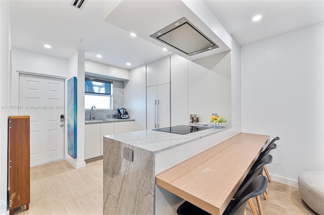 kitchen with a kitchen bar, light wood-type flooring, black electric cooktop, sink, and white cabinets