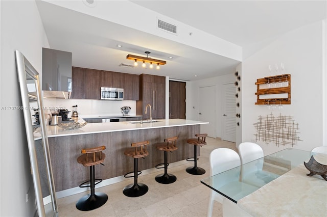 kitchen featuring kitchen peninsula, dark brown cabinetry, extractor fan, sink, and a breakfast bar area