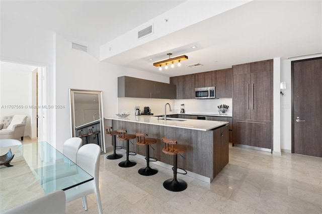 kitchen featuring a kitchen bar, kitchen peninsula, sink, and dark brown cabinets