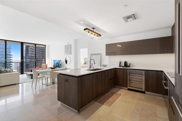 kitchen featuring dark brown cabinets, kitchen peninsula, sink, and wine cooler