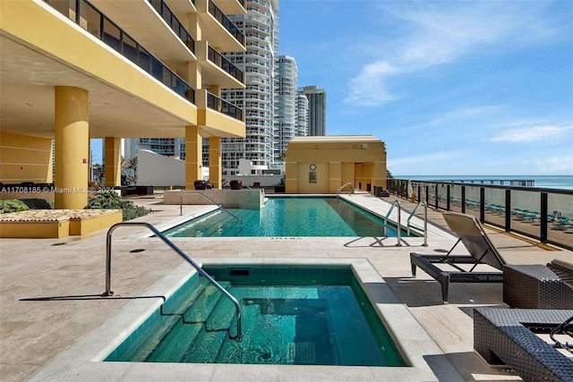 view of swimming pool featuring a patio, a water view, and a hot tub