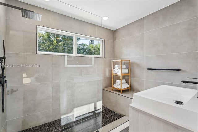 bathroom with tiled shower, vanity, and tile walls