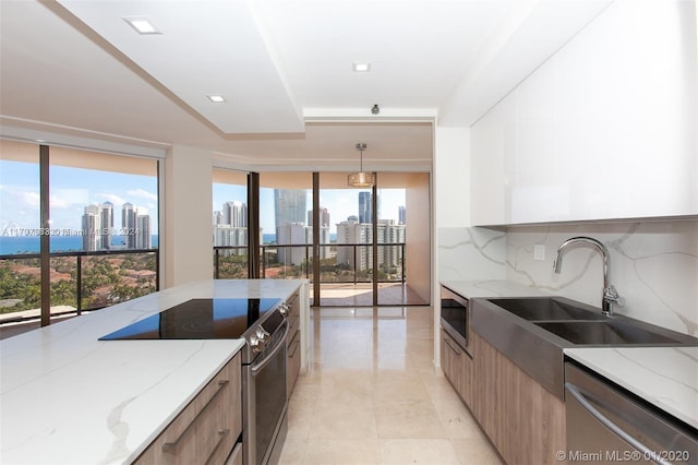 kitchen with decorative backsplash, appliances with stainless steel finishes, light stone counters, sink, and pendant lighting