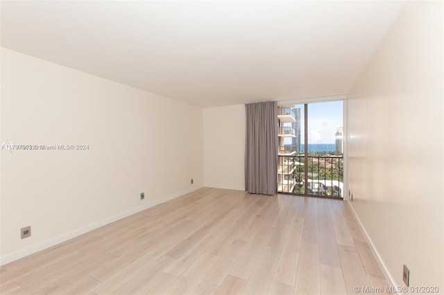 spare room featuring a wall of windows and light wood-type flooring