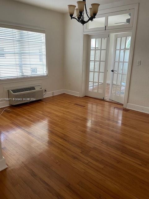 unfurnished room with hardwood / wood-style floors, a notable chandelier, a wall unit AC, and french doors