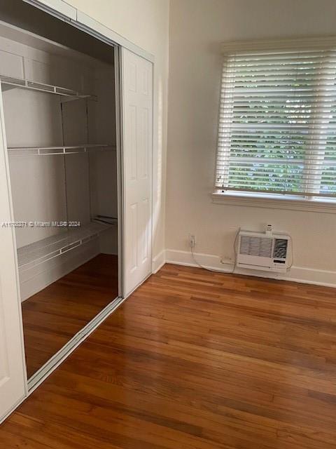 unfurnished bedroom with a wall mounted air conditioner, wood-type flooring, and a closet