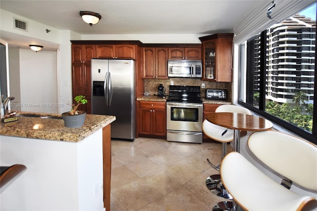 kitchen featuring light tile patterned flooring, sink, light stone counters, tasteful backsplash, and appliances with stainless steel finishes