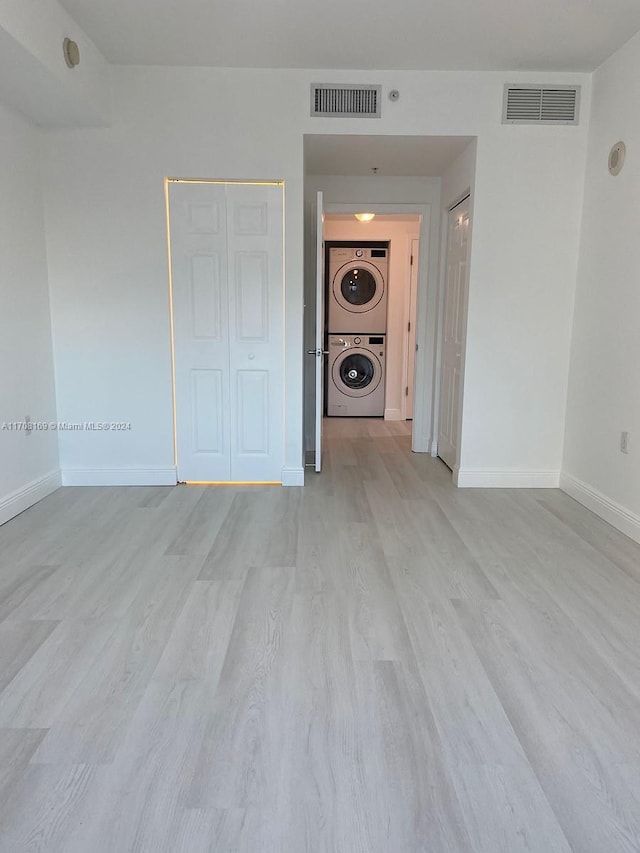 unfurnished room with light hardwood / wood-style floors and stacked washer and dryer