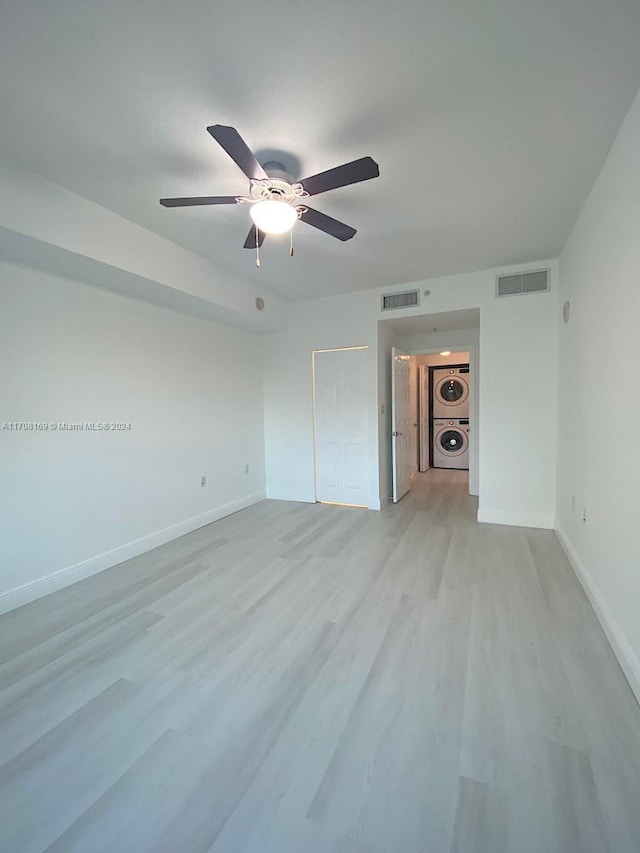 empty room with stacked washer / drying machine, light hardwood / wood-style floors, and ceiling fan