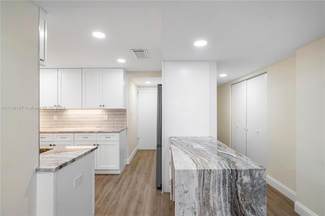 kitchen featuring white cabinetry, a center island, tasteful backsplash, light stone counters, and light wood-type flooring