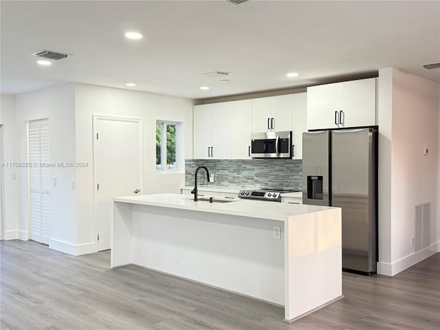 kitchen with light wood-type flooring, stainless steel appliances, a kitchen island with sink, sink, and white cabinets