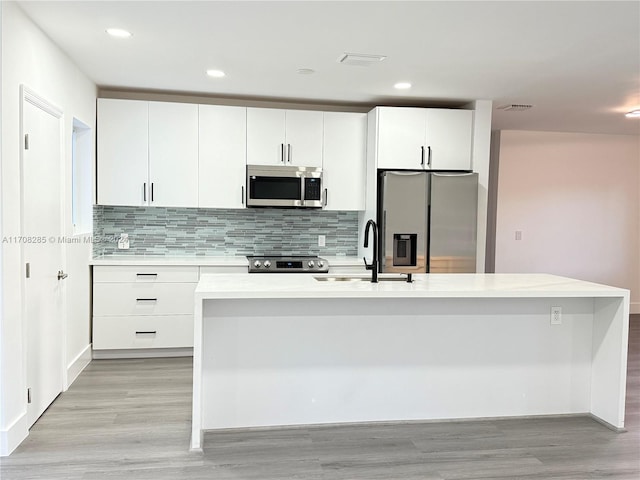 kitchen with sink, an island with sink, light hardwood / wood-style floors, white cabinets, and appliances with stainless steel finishes