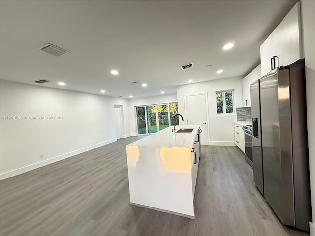 kitchen featuring a kitchen island with sink, stainless steel refrigerator with ice dispenser, decorative backsplash, light hardwood / wood-style floors, and white cabinetry