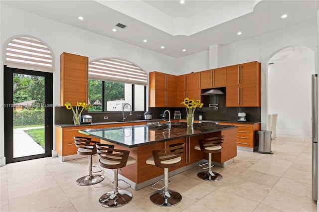 kitchen with decorative backsplash, a kitchen bar, dark stone counters, sink, and a center island with sink