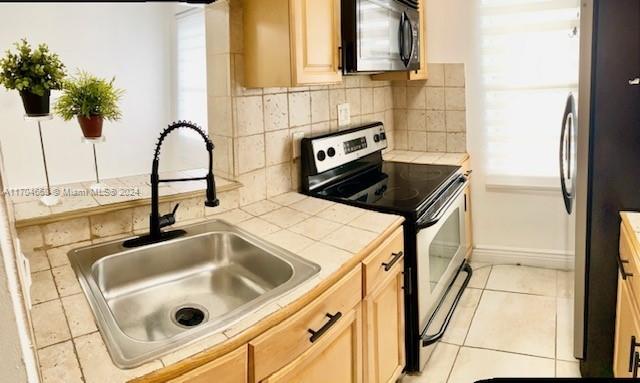 kitchen with light brown cabinetry, stainless steel appliances, sink, light tile patterned floors, and tile countertops