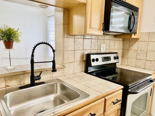 kitchen featuring light brown cabinetry, tile countertops, stainless steel electric range oven, and sink