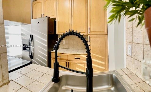 interior details with backsplash, tile countertops, light brown cabinets, and sink