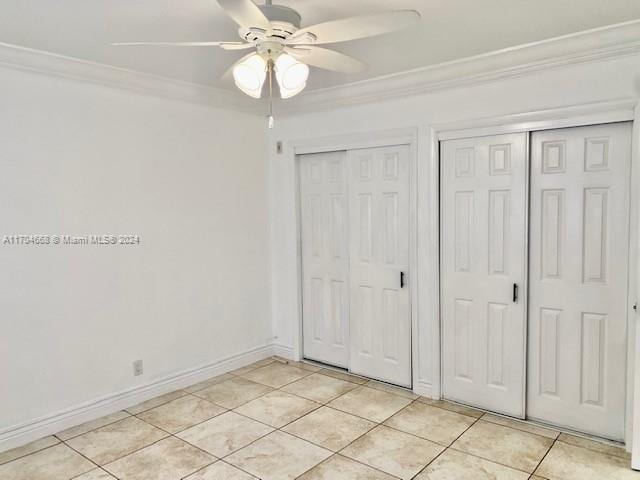 unfurnished bedroom featuring crown molding, ceiling fan, multiple closets, and light tile patterned flooring