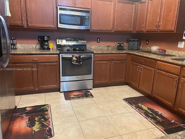 kitchen with light stone countertops, sink, light tile patterned floors, and stainless steel appliances