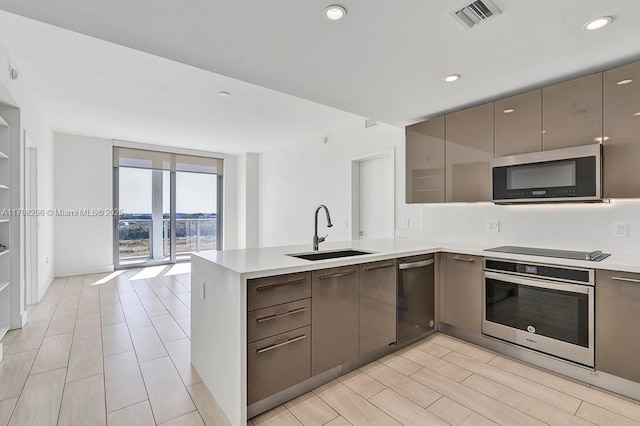 kitchen with sink, expansive windows, kitchen peninsula, oven, and black electric cooktop