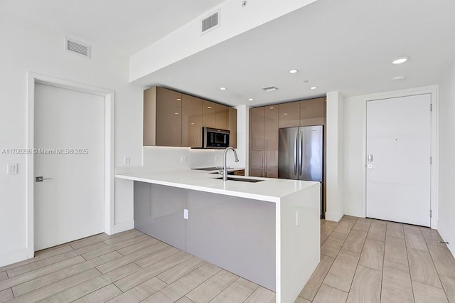 kitchen with stainless steel refrigerator, kitchen peninsula, sink, and a kitchen bar