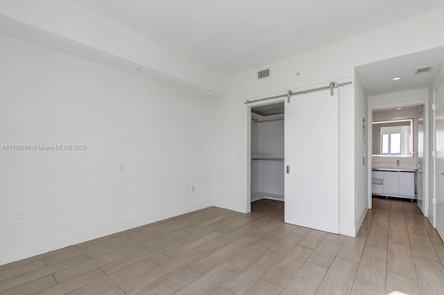 unfurnished bedroom with a spacious closet, a barn door, ensuite bathroom, light hardwood / wood-style floors, and a closet