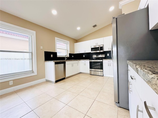 kitchen featuring stainless steel appliances, lofted ceiling, white cabinetry, and light stone countertops