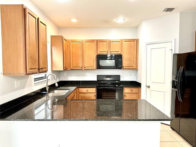 kitchen with dark stone counters, black appliances, sink, light tile patterned floors, and kitchen peninsula