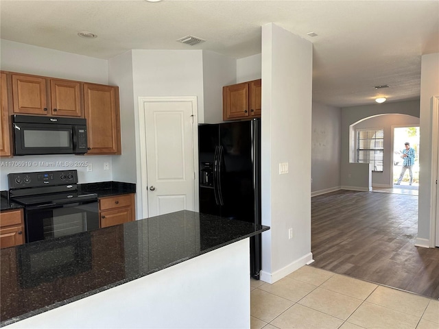 kitchen with light tile patterned floors, black appliances, and dark stone counters