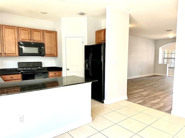 kitchen with dark stone countertops, light tile patterned floors, and black appliances