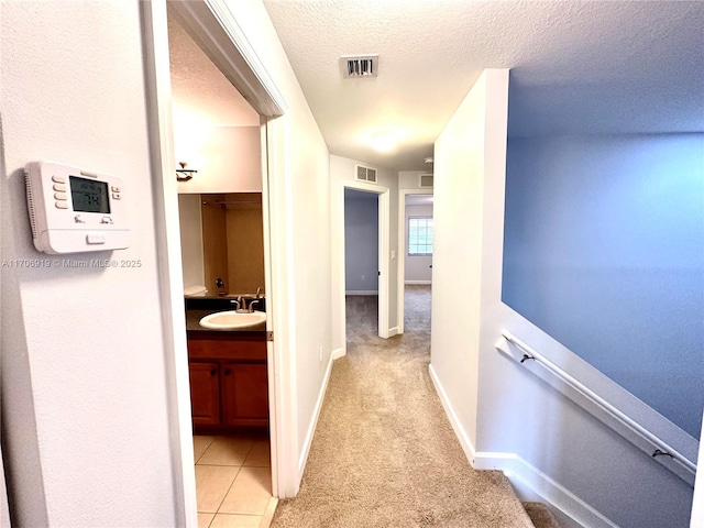 corridor with light carpet, sink, and a textured ceiling