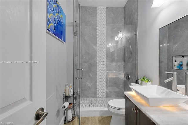 bathroom with toilet, wood-type flooring, a shower with shower door, and vanity