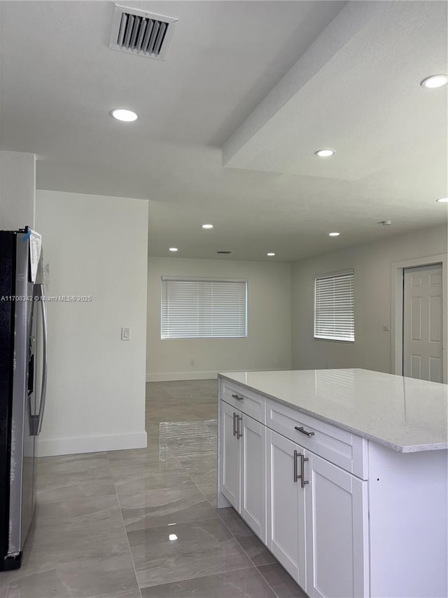 kitchen with stainless steel fridge, white cabinetry, and light stone counters