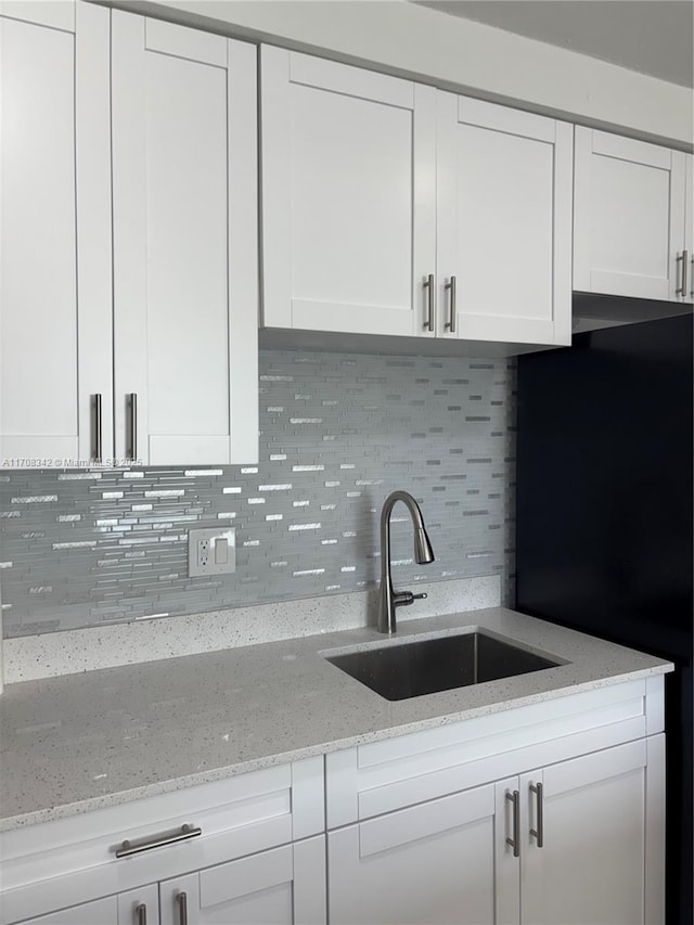 kitchen with decorative backsplash, black refrigerator, light stone counters, sink, and white cabinetry