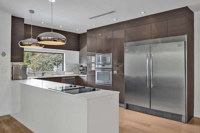 kitchen featuring light wood-type flooring, dark brown cabinets, sink, built in appliances, and hanging light fixtures