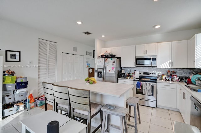 kitchen with visible vents, light tile patterned flooring, stainless steel appliances, white cabinets, and a kitchen bar